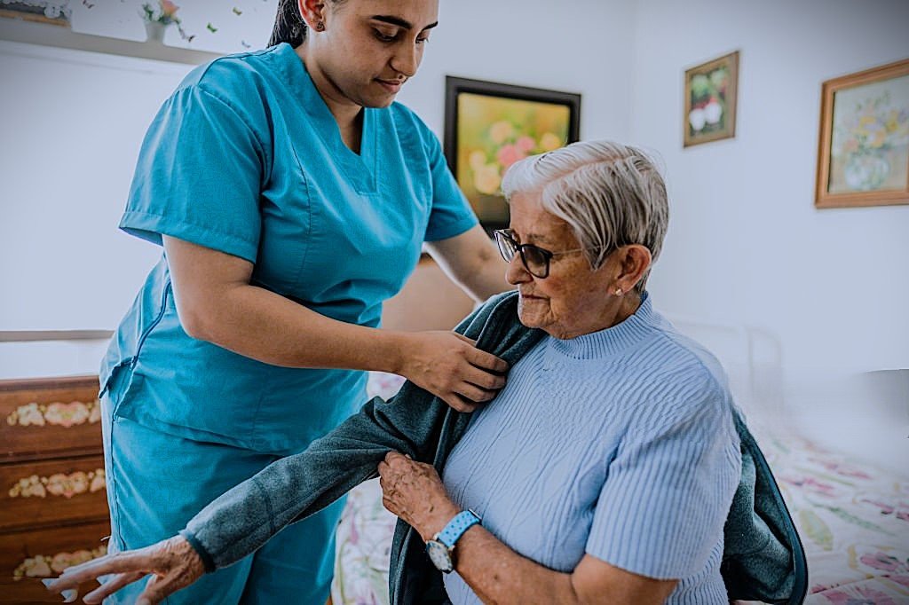 CareNestPro Caregiver helping senior woman put on coat at home